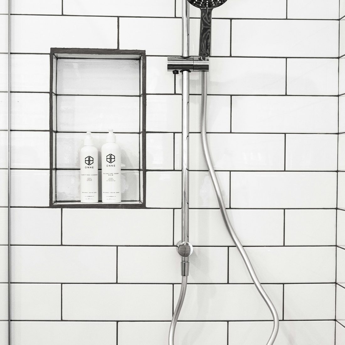 Close-up of white subway-tile shower wall with dark grout and chrome fittings