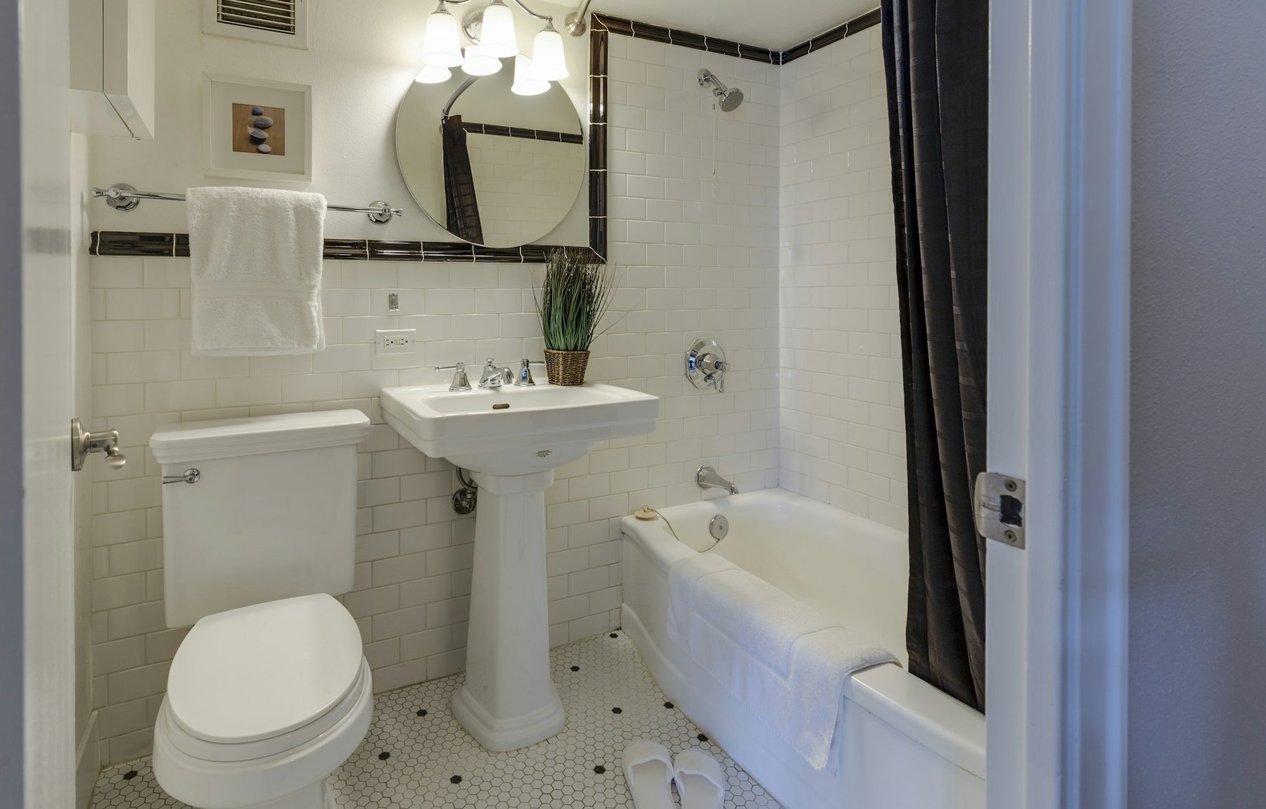 Freshly tiled white subway-tile bathroom with pedestal basin and bath, dark trim accents